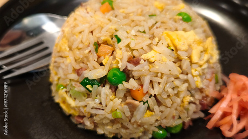 Close-up of Japanese-style fried rice (Chahan) with diced chashu pork, egg, peas, and carrots, served with pickled ginger on a black plate