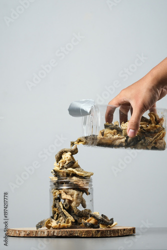 Hand pours crunchy salmon fish skin snacks into a clear jar.