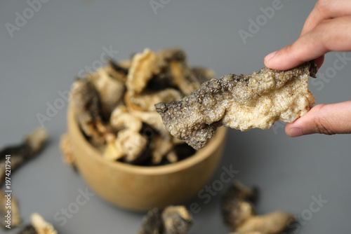 Person holds fried salmon fish skin over a bowl. Suitable for seafood lovers, food bloggers, restaurant menus, and cooking related designs.