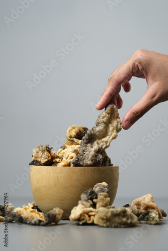 Person holds fried salmon fish skin over a bowl. Suitable for seafood lovers, food bloggers, restaurant menus, and cooking related designs.