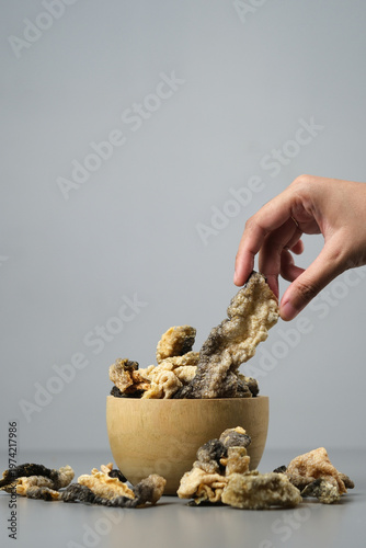 Person holds fried salmon fish skin over a bowl. Suitable for seafood lovers, food bloggers, restaurant menus, and cooking related designs.