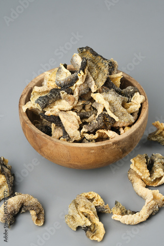 Wooden bowl showcases crispy salmon skin chips on gray surface. Perfect for food blogs, menus, snack packaging, culinary websites.