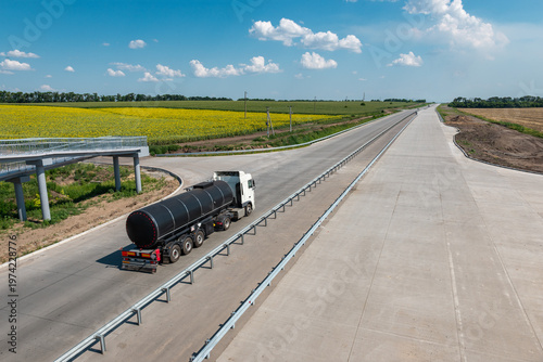 Black tanker truck on highway with colorful fields around