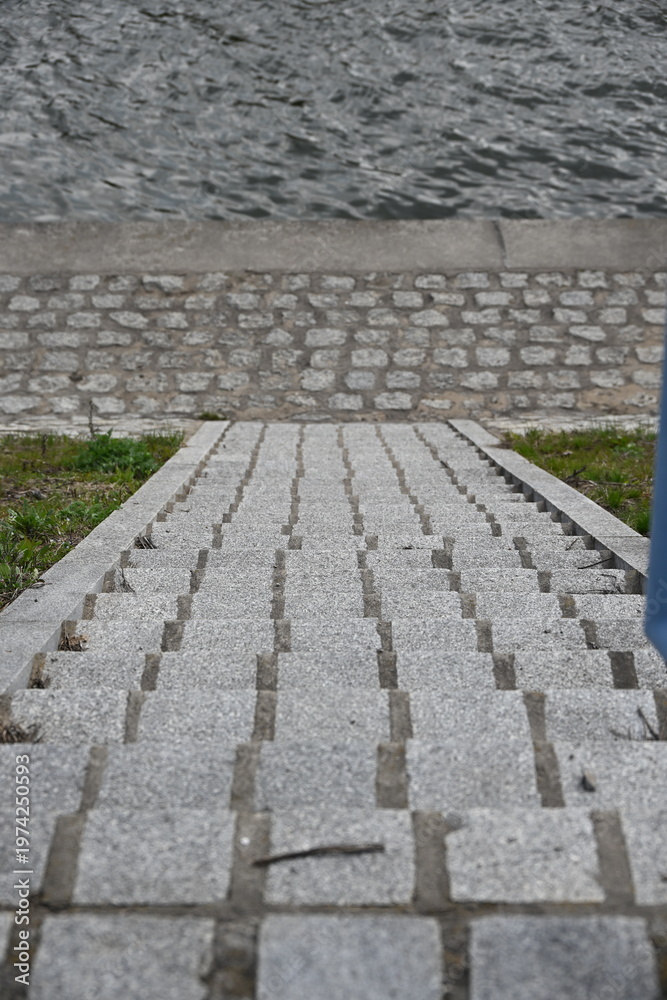 Fototapeta premium Stone steps leading to cobblestone riverside walkway along calm river water