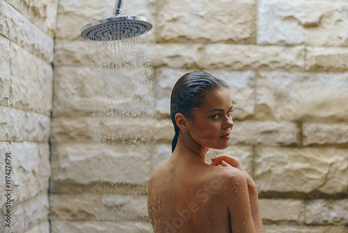 woman taking outdoor shower with stone wall background, wet hair, natural light, refreshing moment, calm expression, spa atmosphere