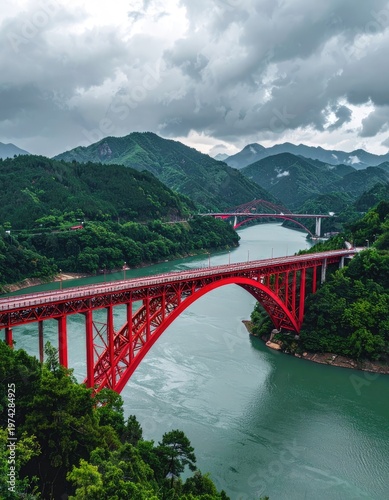 A vibrant red arch bridge gracefully spans a winding river amidst lush green mountains under a cloudy sky.