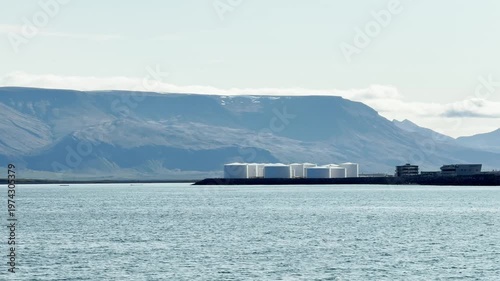Seascape, horizon view of huge white tanks, oil and fuel storage facilities, mountain on the horizon, industrial Iceland landscape.