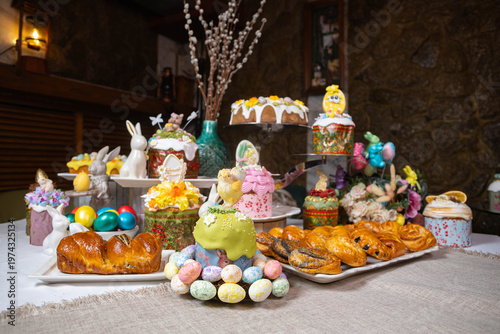 Festive Easter dessert table with colorful cakes, eggs, and floral decorations on stone wall