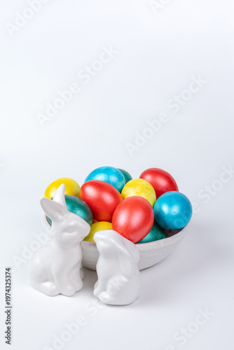 White Porcelain Bunnies and Painted Easter Eggs in Ceramic Bowl on White Background