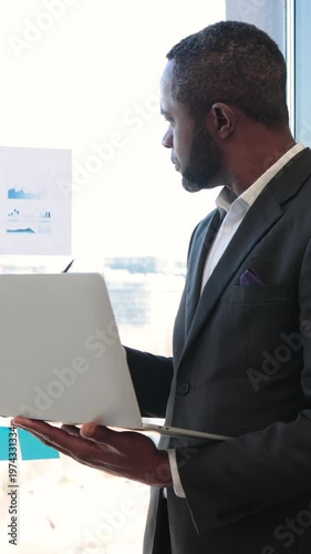 An African American businessman reviews financial charts and graphs while holding a laptop, indicating a focus on data-driven decision-making