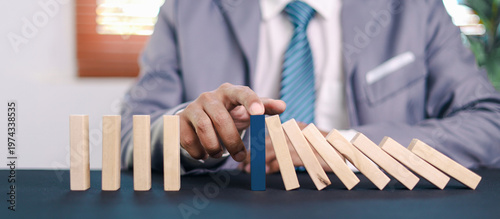 Businessman hand stopping falling domino blocks to prevent chain reaction, symbolizing risk control, leadership, and strategic decision making