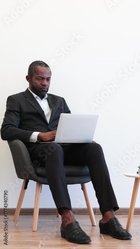 An African American man in a suit sits thoughtfully with a laptop on his lap, contemplating his next move