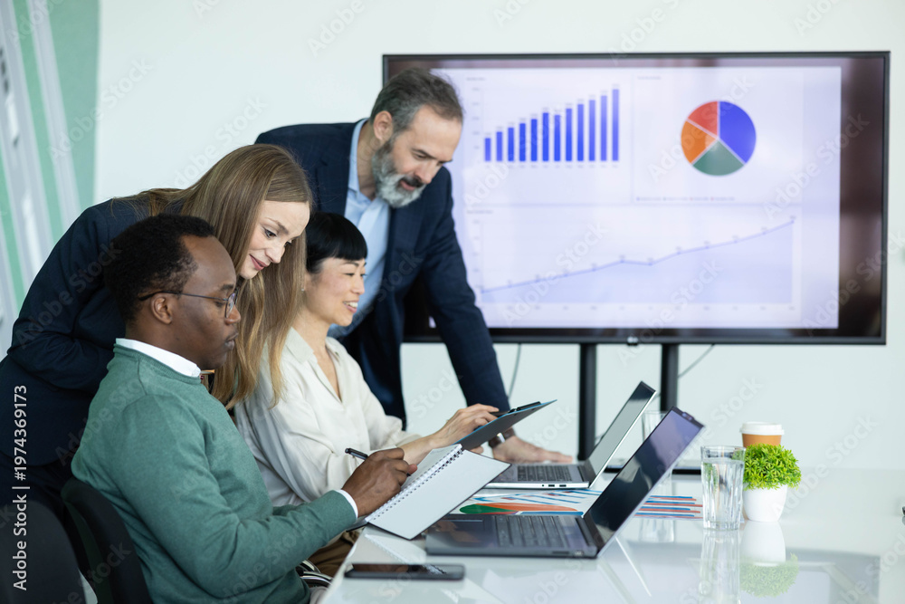 Naklejka premium Multicultural business team working together in an office meeting, reviewing financial data and charts on a large screen