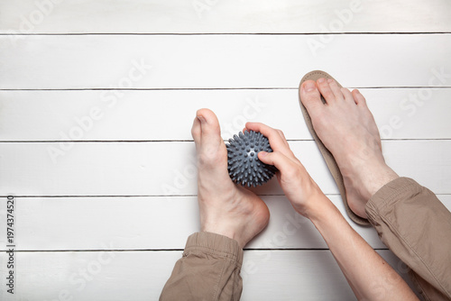 Top view of hand massaging foot with gray ball and orthopedic insoles on white wooden background with copy space