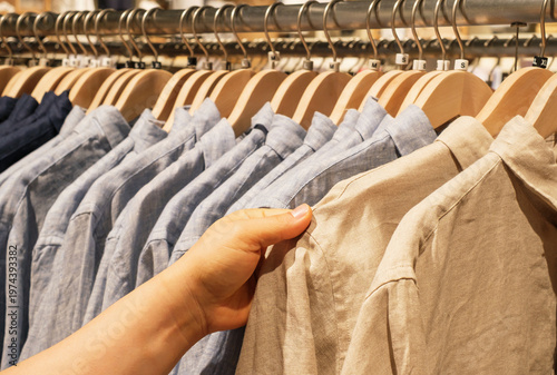 Man chooses a shirt hanging on hanger in store, side view.