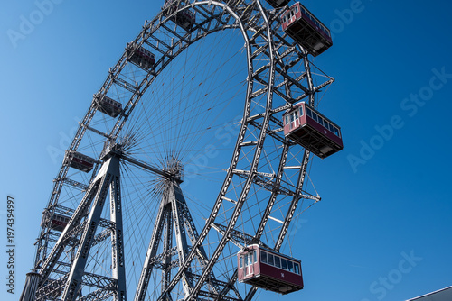 Vienna, Austria – Looking up at the giant steel structure and vintage red gondolas of the Wiener Riesenrad Ferris wheel against a deep blue sky.