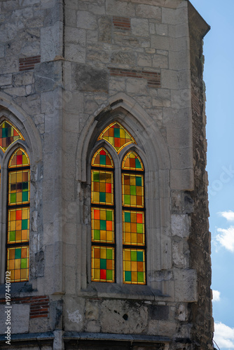 Colorful stained glass window set in a Gothic stone frame, highlighting geometric patterns, weathered masonry and historic architectural detail.