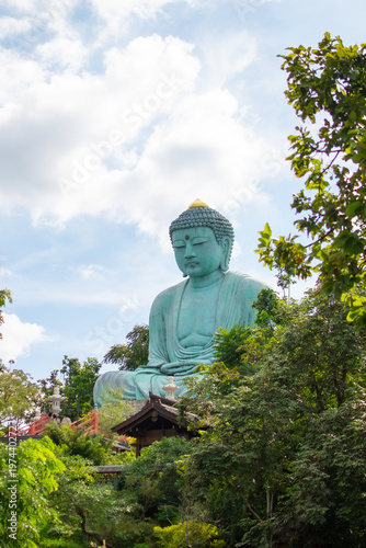 Large Great Buddha statue surrounded by green trees under cloudy sky