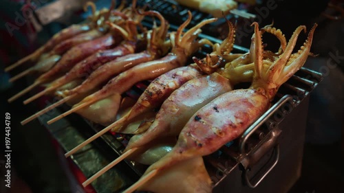 Close-up view of fresh whole squid on bamboo skewers being grilled over hot charcoal at a street food stall
