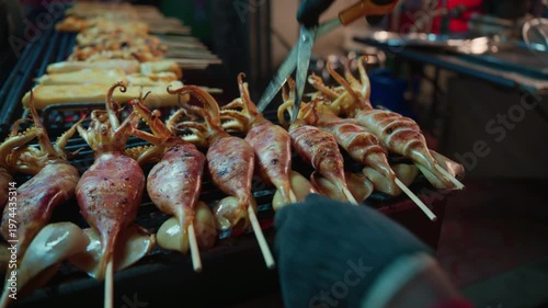 Close-up of a street food vendor using scissors to cut grilled squid on skewers at a night market in Bangkok, Thailand
