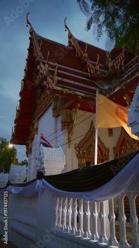 Vertical shot of a traditional Thai Buddhist temple illuminated at dusk with waving flags, Bangkok, Thailand