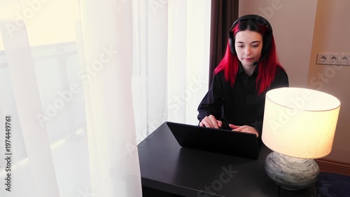 Focused woman is using computer wearing headset and talking during video call. Young adult Caucasian lady is engaged in remote job. Dedicated afterhours support scene theme. Freelancer concept