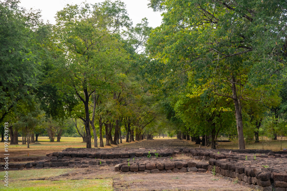 Fototapeta premium Ancient brick ruins at Khao Khlang Nok in Thailand, a historic archaeological site surrounded by trees under a blue sky with clouds