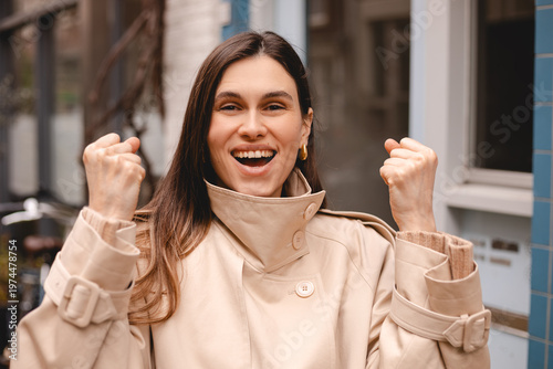 Konstfotografi Portrait of a happy successful young woman in beige trench coat looking at camer