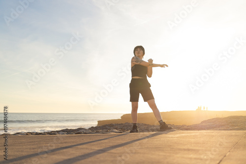Woman stretching arm performing outdoor exercise at sunset