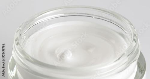 Open jar with cosmetic facial cream close-up on a rotating table. Lid is being removed from the jar of cosmetic cream.