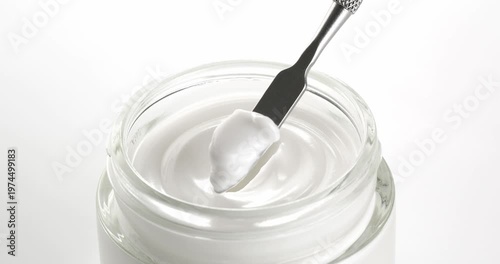 Open jar of cosmetic facial cream. Cream is scooped from the jar with a cosmetic spatula.