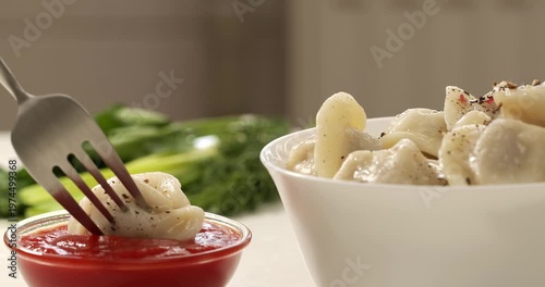 Freshly cooked dumplings are picked up with a fork and dipped in ketchup, close-up footage, dill in the background.