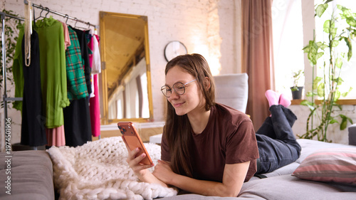 Photos Woman lying on sofa using smartphone for online shopping in cozy apartment