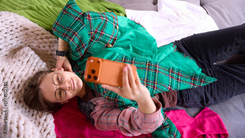 Quadro su tela Woman taking selfie while lying on sofa with green jacket and colorful clothes