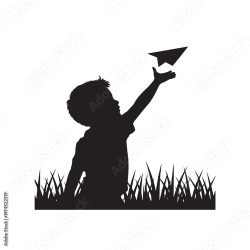Silhouette of a young boy in grass throwing a paper airplane with outstretched hand reaching upwards towards the sky