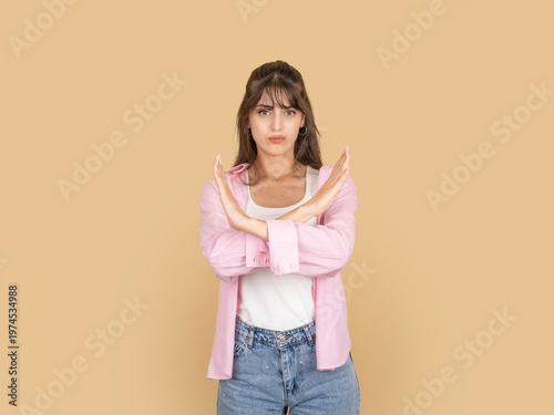 Photos Serious caucasian woman making stop gesture with crossed arms, expressing rejection or refusal concept idea image, wearing pink shirt, isolated on beige studio background with copy space