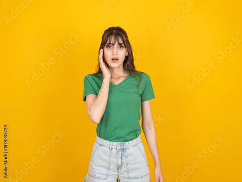 Foto Shocked caucasian woman touching face with hand, reacting with surprise and disbelief concept idea image, wearing green t-shirt, isolated on bright yellow studio background with copy space