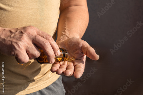 Close up view of a person's hands pouring essential dietary supplements, such as vitamins or omega-3, from a bottle. Man pouring yellow softgel capsules into hand. Healthy lifestyle, self-care