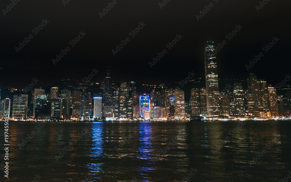 Obraz premium Hong Kong cityscape glows brightly at night over Victoria Harbour, displaying many tall buildings and water reflections
