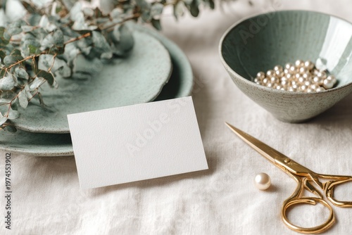 Flat lay of an empty white card with ceramic dishes, eucalyptus, pearls, and scissors