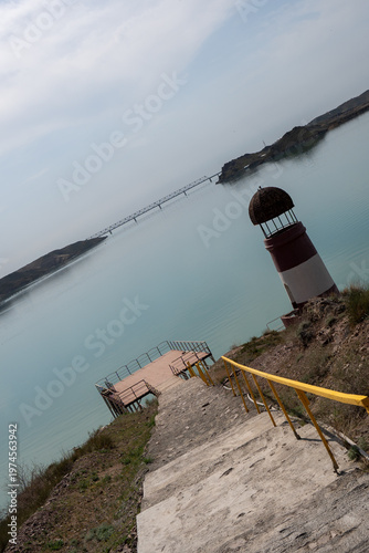 Solitary lighthouse on a pier surrounded by turquoise water. Qonayev, Central Asia