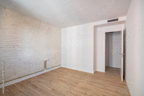 Empty room with white walls and wooden floor. A door leads to another space. The room has a minimalist design and natural light.