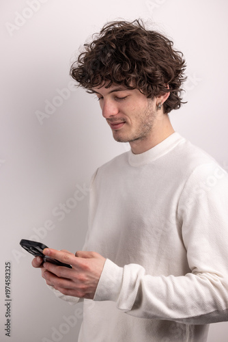 Fotografie Jeune homme concentré utilisant son smartphone, illustrant la communication digitale et les usages quotidiens de la technologie dans un cadre épuré