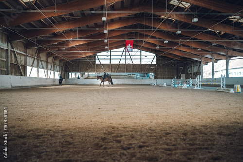 Vászonkép Horses training in an indoor arena with sand footing and a swiss flag overhead
