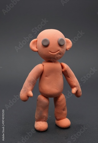 Clay figurine toy character smiling minimalist orange humanoid sculpture against dark gray studio background