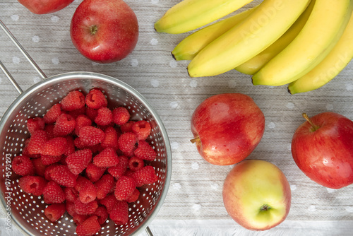 Fresh raspberries with apples and bananas on table. 