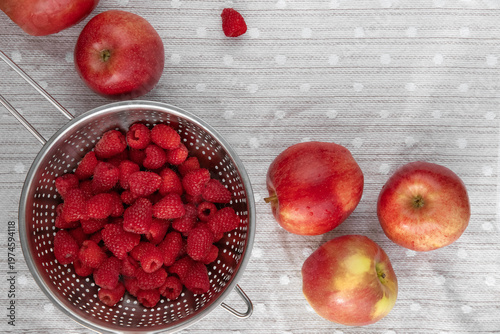 Raspberries and apples arranged on light surface. 