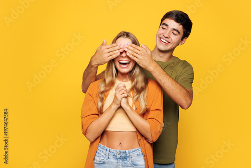 Young fun couple two friends family man woman wear shirt casual clothes cuddle embrace together close eyes with hands play guess who or hide and seek isolated on pastel plain yellow background studio.