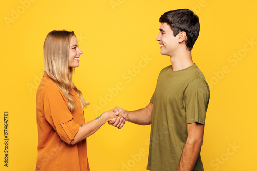 Side view calm young smiling happy couple two friends family man woman wear casual clothes looking to each other shaking hands together isolated on plain light yellow color background studio portrait.