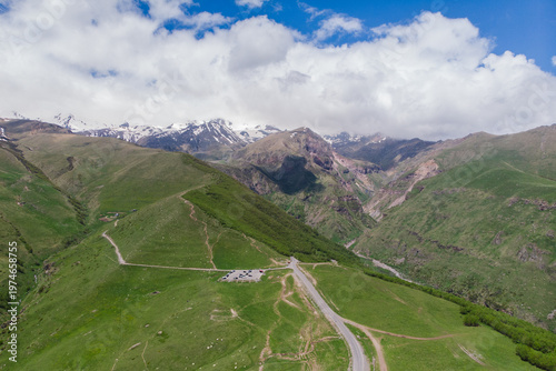 Aerial View of Kazbegi Mountains in Georgia, Winding Road and Green Hills Landscape, Snow-Capped Caucasus Peaks. Adventure Travel and Tourism Concept, Majestic Nature Scene with Clouds and Sky